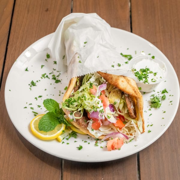 Liberty's Mediterranean Giant Grinder, a gyro with meat, lettuce, tomatoes, onions, and sauce, on a white plate.
