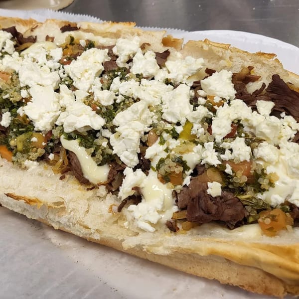 Close-up of a Mediterranean Giant Grinder with steak, feta, and green relish on a white plate.