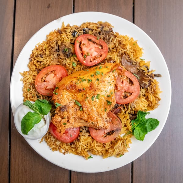 Liberty’s Mediterranean Giant Grinders' chicken and rice dish with tomato slices and a side of yogurt sauce.