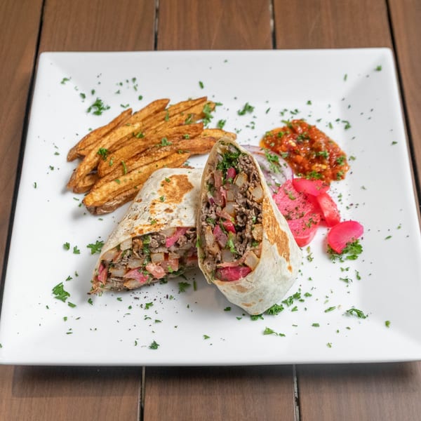 A Mediterranean grinder, cut in half, with fries, salsa, and pickled turnips on a white plate.