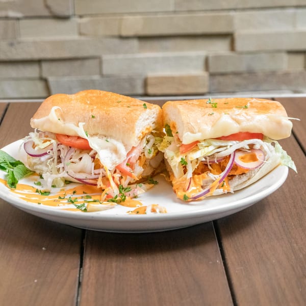 A Mediterranean Giant Grinder, cut in half, filled with meat, cheese, lettuce, tomato, and onion.