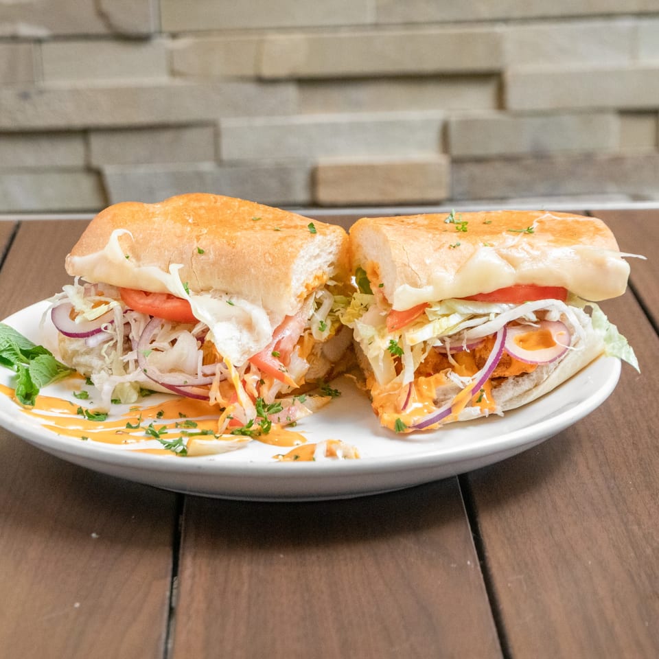 A Mediterranean Giant Grinder, cut in half, filled with meat, cheese, lettuce, tomato, and onion.