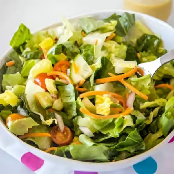 A fresh Mediterranean salad with lettuce, tomatoes, cucumbers, and shredded carrots in a white bowl.