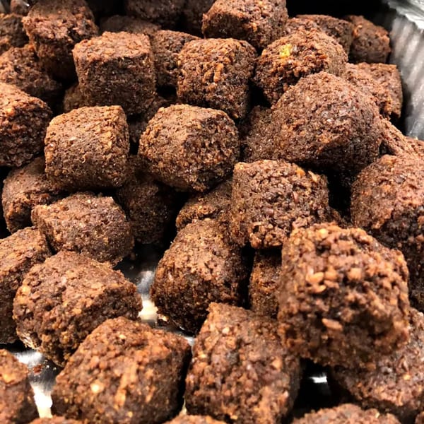 Close-up of numerous dark brown, square-shaped falafel pieces with a textured, crispy coating.