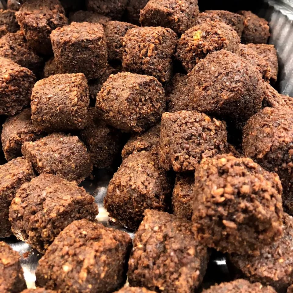 Close-up of numerous dark brown, square-shaped falafel pieces with a textured, crispy coating.